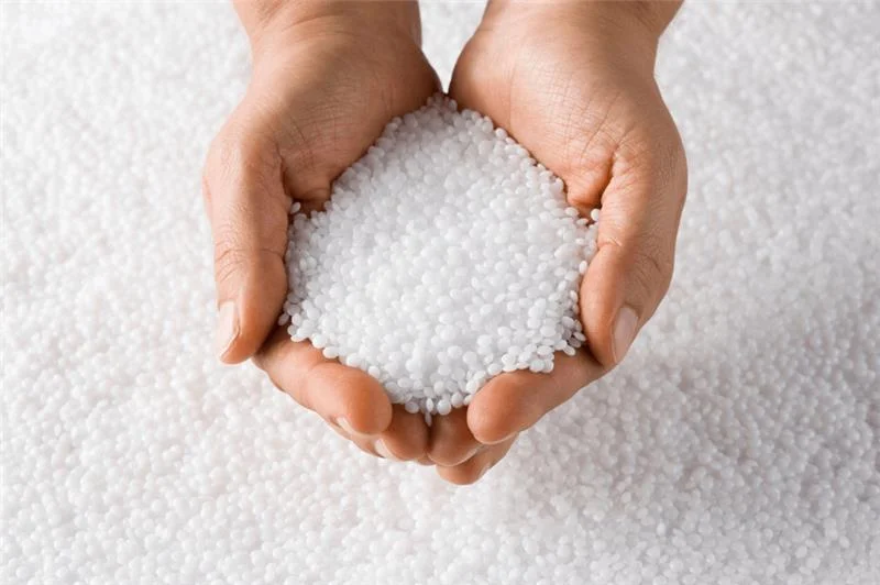 Hands holding white plastic resin pellets, raw material for packaging products and recycled content manufacturing.