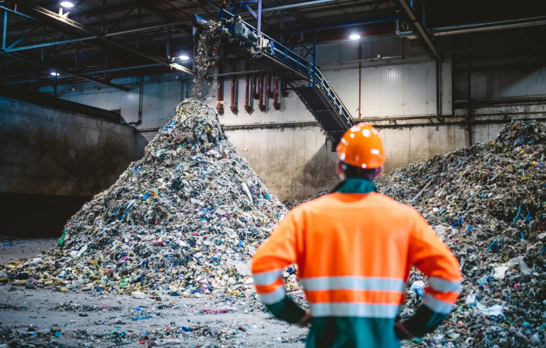 A worker stands before a large pile of plastic waste, highlighting landfill issues addressed by California’s Plastic Bag Ban.