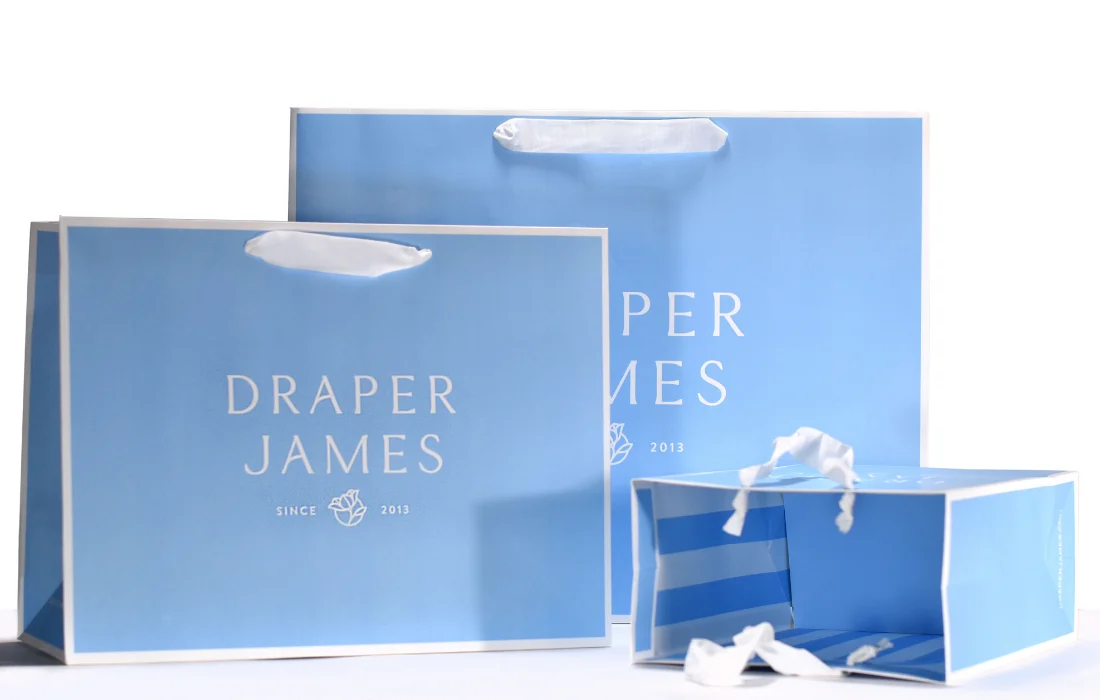 Blue branded paper shopping bags illustrate compliant reusable bag options under California’s Plastic Bag Ban.