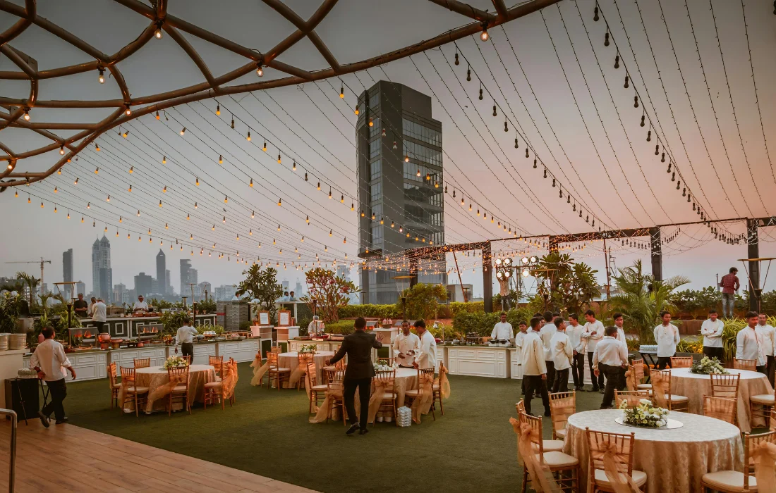 Rooftop catering event setup at sunset with tables, staff, and city skyline in the background.