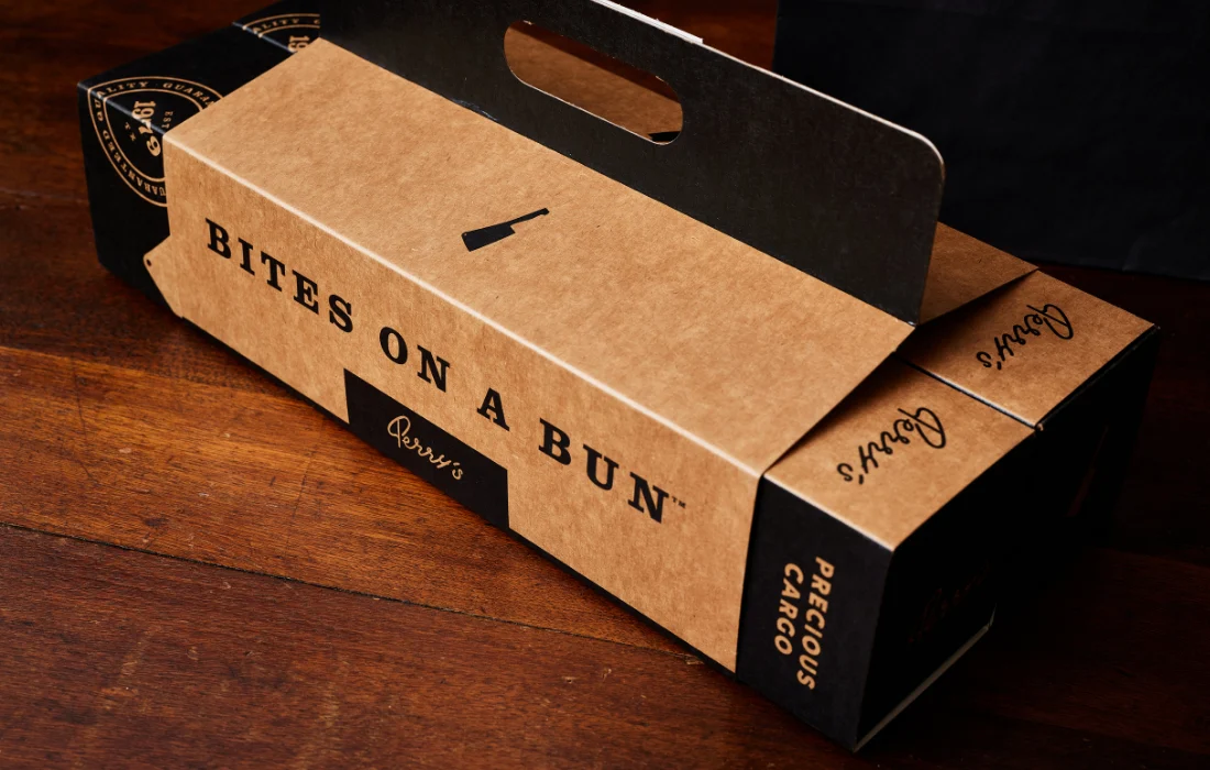 Stylish branded paper catering box and bags from Perry’s Steakhouse on a wooden table.