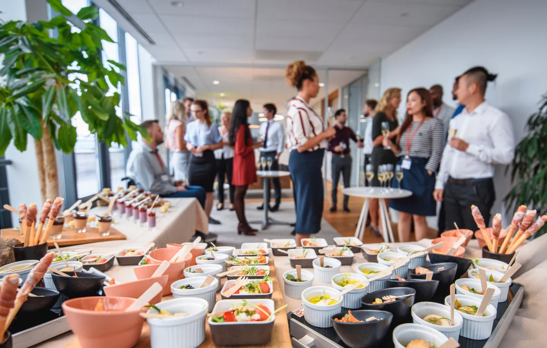 Corporate catering buffet with assorted appetizers and professionals networking in the office.