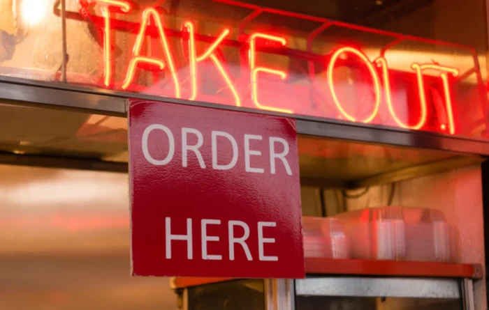 Neon takeout sign with an “Order Here” label at a restaurant counter for to-go food containers and takeout orders.