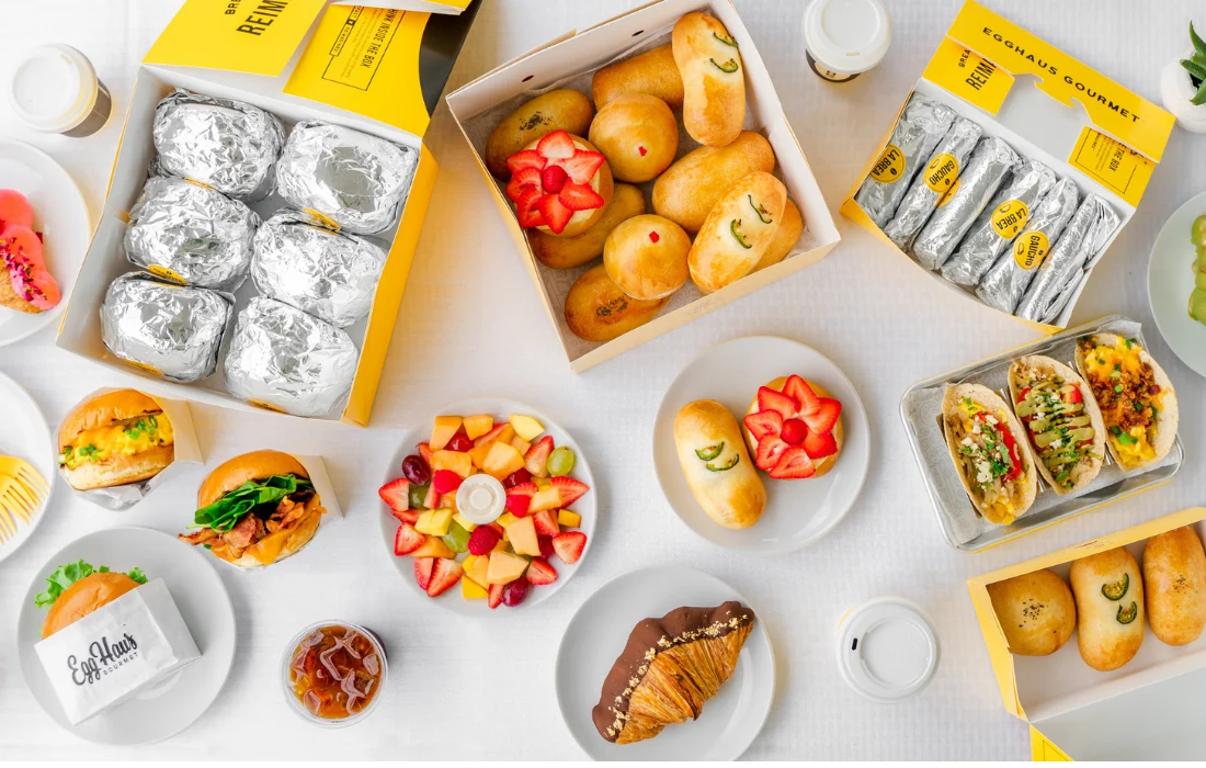 Breakfast takeout boxes with sandwiches, tacos, pastries, and fruit in eco-friendly to-go packaging for catering.