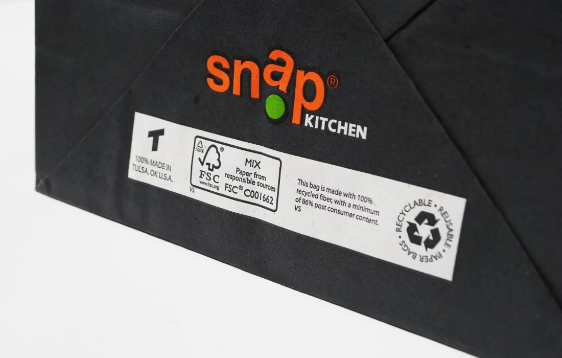 Black Snap Kitchen paper to-go bag made from 100% recycled materials, emphasizing eco-friendly takeout packaging.