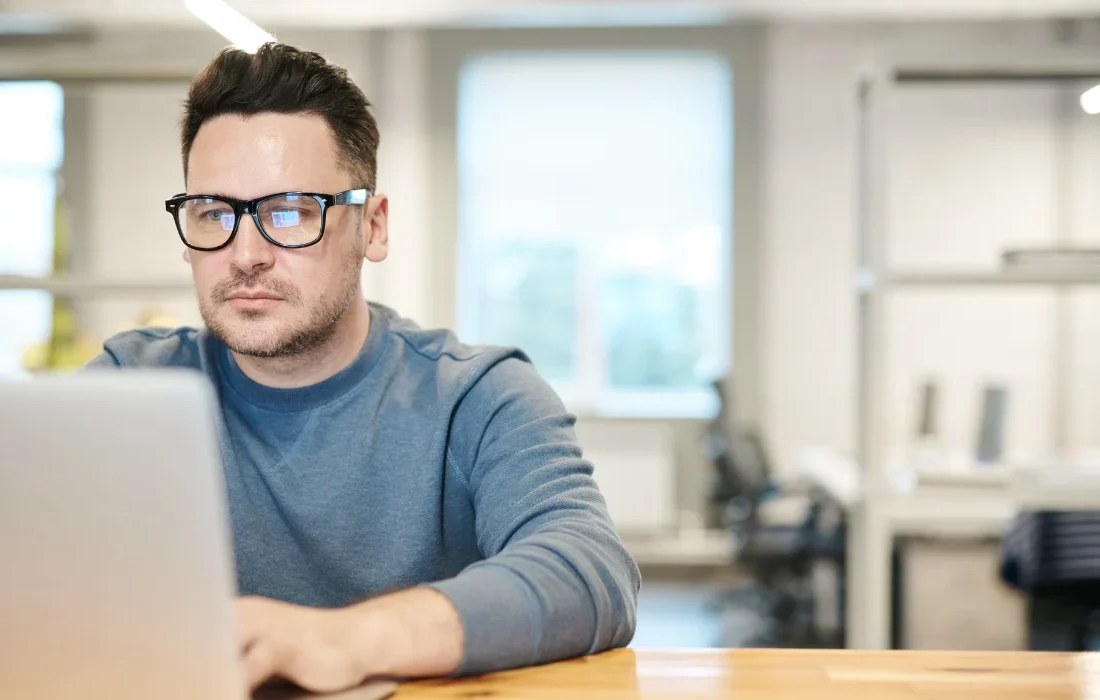 Man working on a laptop in a modern office while researching sustainable packaging information and compliance requirements.