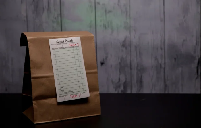 Brown kraft paper takeout bag with a restaurant guest check stapled to the top.
